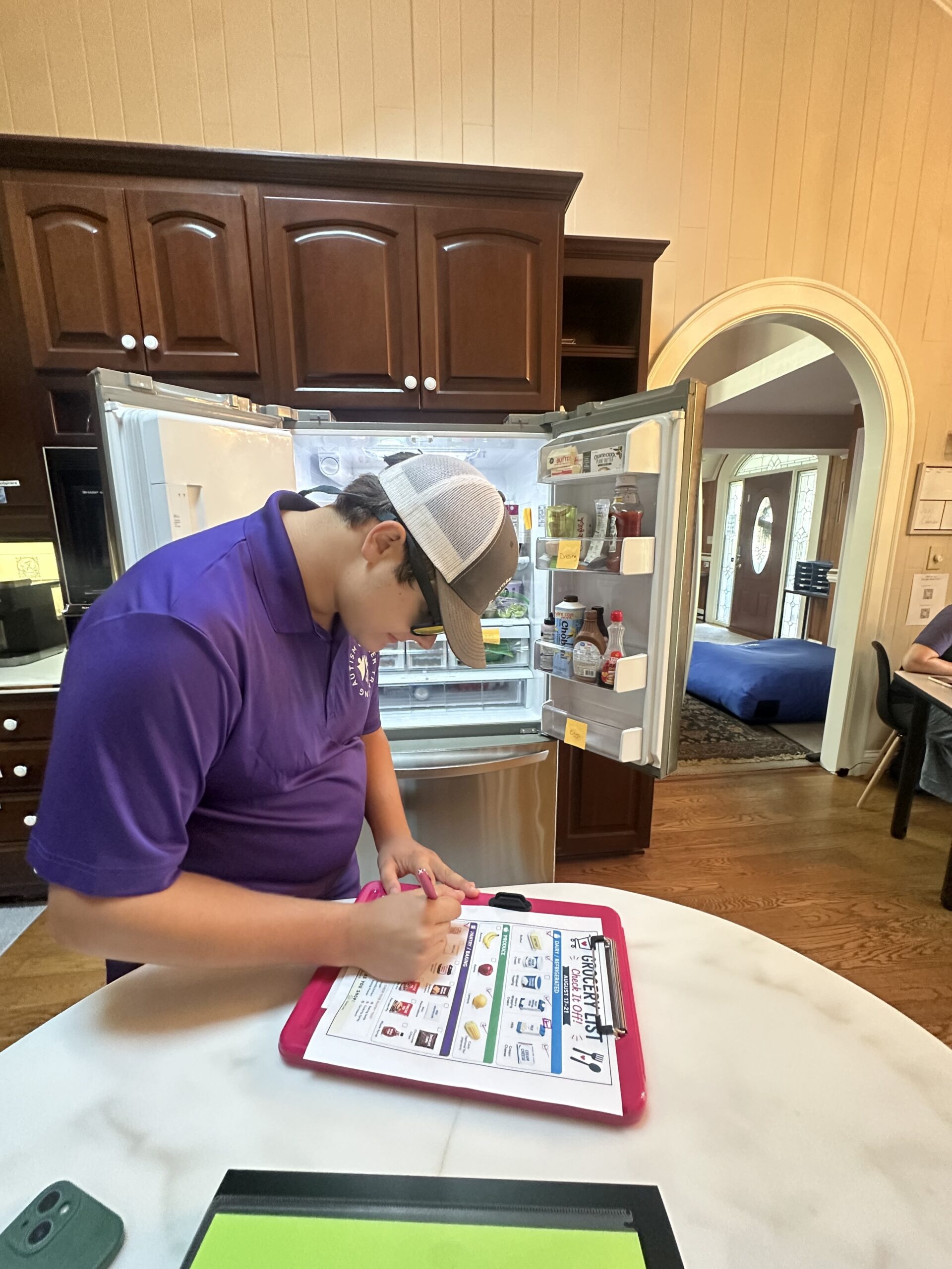 Trainee completing a grocery checklist beside an open refrigerator